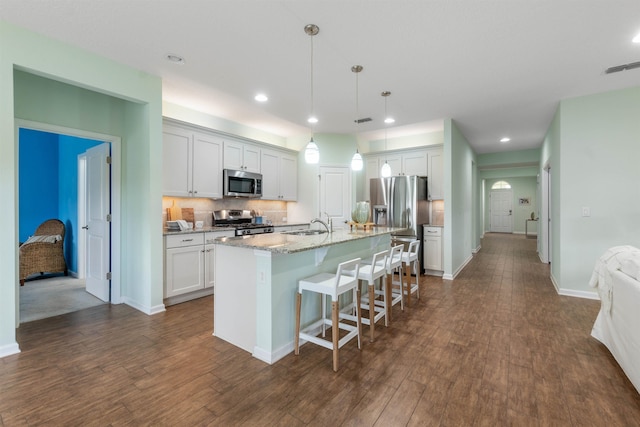 kitchen featuring dark wood finished floors, stainless steel appliances, decorative backsplash, an island with sink, and a kitchen breakfast bar