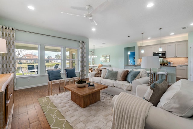 living room featuring baseboards, light wood-type flooring, visible vents, and recessed lighting