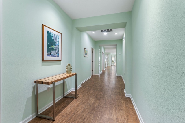 hall with dark wood-type flooring, visible vents, and baseboards