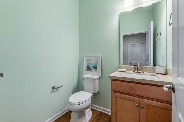 half bathroom with toilet, baseboards, wood finished floors, and vanity