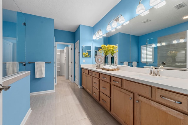 bathroom featuring double vanity, tiled shower, a sink, and visible vents