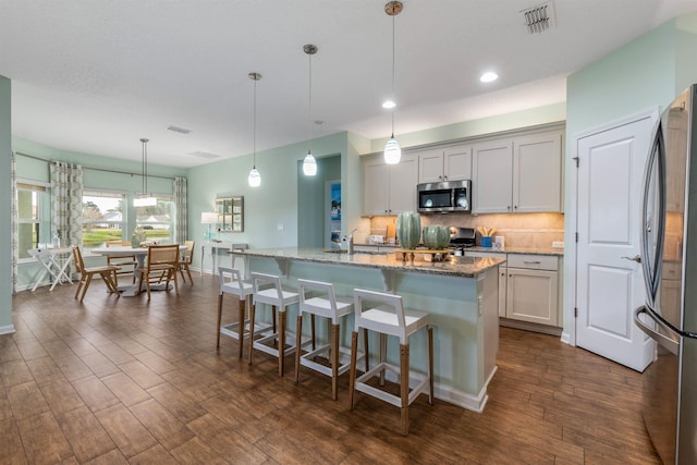 kitchen featuring light stone counters, visible vents, appliances with stainless steel finishes, dark wood-style floors, and tasteful backsplash