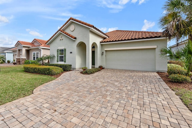 mediterranean / spanish-style house featuring a garage, a tiled roof, decorative driveway, a front lawn, and stucco siding