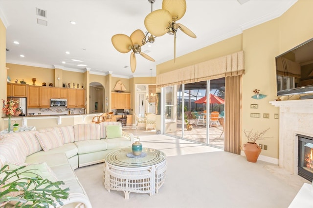 carpeted living room with a high end fireplace, ceiling fan, and crown molding