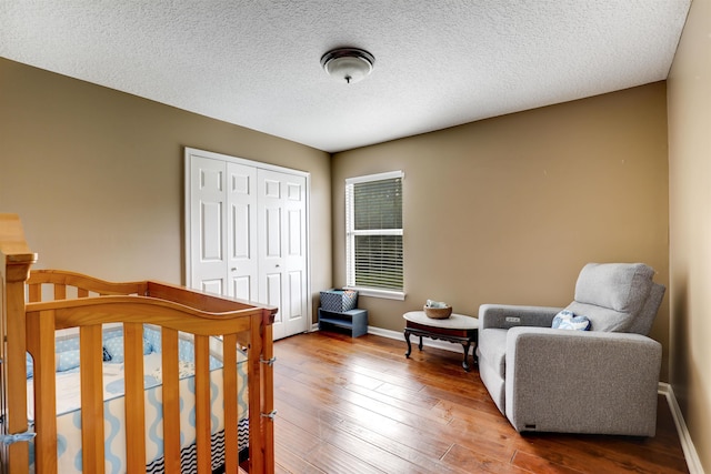 bedroom with a crib, a textured ceiling, hardwood / wood-style flooring, and a closet