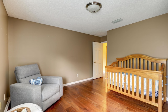 bedroom featuring wood-type flooring, a textured ceiling, and a nursery area