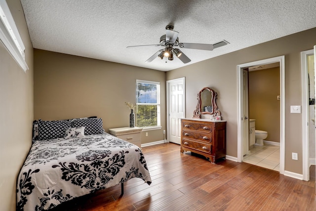 bedroom featuring ceiling fan, ensuite bathroom, a textured ceiling, and light wood-type flooring