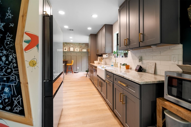 kitchen featuring backsplash, light hardwood / wood-style floors, light stone counters, and sink