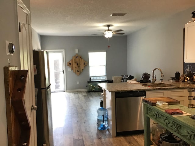 kitchen featuring appliances with stainless steel finishes, a textured ceiling, sink, wood-type flooring, and white cabinets