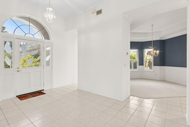 entryway featuring a chandelier, visible vents, light tile patterned flooring, ornamental molding, and light carpet