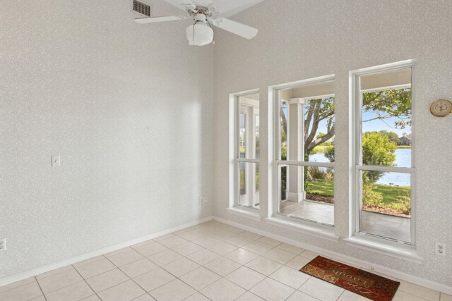 spare room with light tile patterned floors, visible vents, a water view, baseboards, and a ceiling fan
