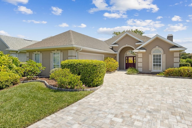 single story home featuring a chimney, decorative driveway, stucco siding, a front lawn, and a garage