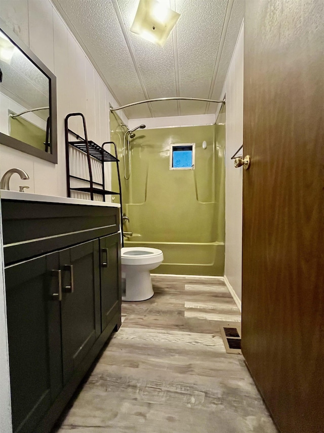 full bath featuring toilet, a textured ceiling, wood finished floors, shower / washtub combination, and vanity