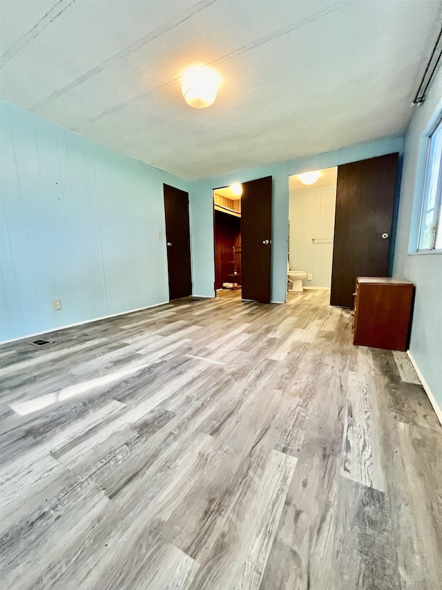 unfurnished bedroom featuring ensuite bath and wood finished floors