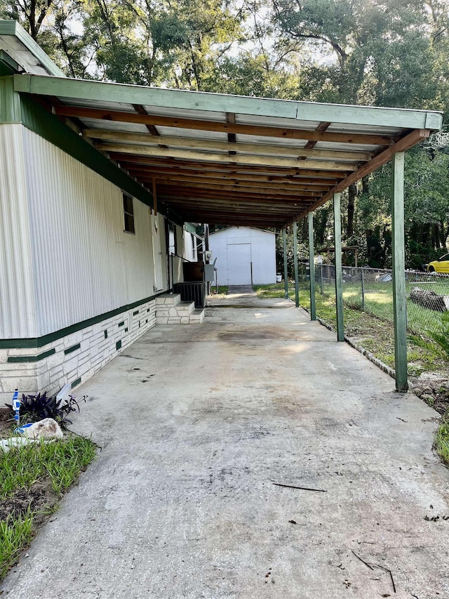 view of vehicle parking with fence, concrete driveway, a carport, and a shed