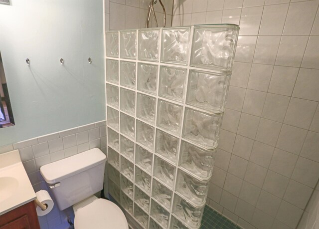 bathroom featuring a tile shower, vanity, toilet, and tile walls