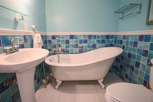 bathroom with a tub to relax in, tile patterned floors, and tile walls