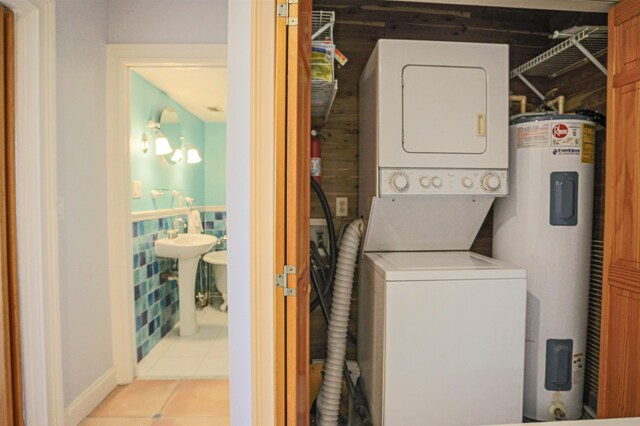 clothes washing area with stacked washer / drying machine, electric water heater, and light tile patterned floors