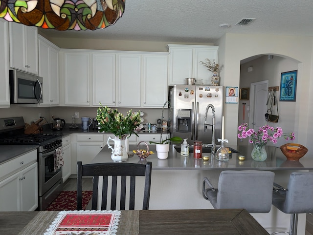 kitchen with a textured ceiling, white cabinetry, and stainless steel appliances