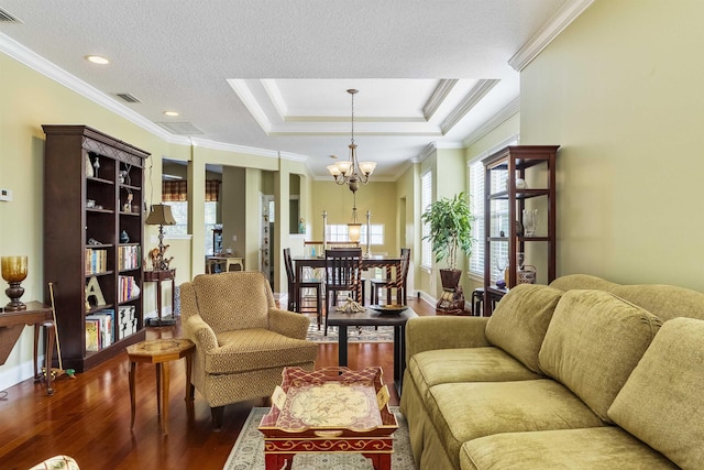 living room with a raised ceiling, dark hardwood / wood-style floors, a chandelier, a textured ceiling, and ornamental molding