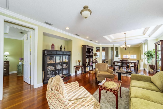 living room with ornamental molding, a textured ceiling, a tray ceiling, dark wood-type flooring, and a chandelier