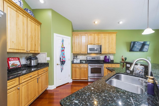 kitchen with stainless steel appliances, sink, dark stone countertops, dark hardwood / wood-style floors, and hanging light fixtures