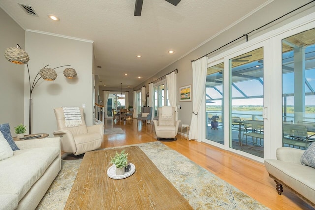 living room featuring wood-type flooring, a textured ceiling, ceiling fan, and ornamental molding