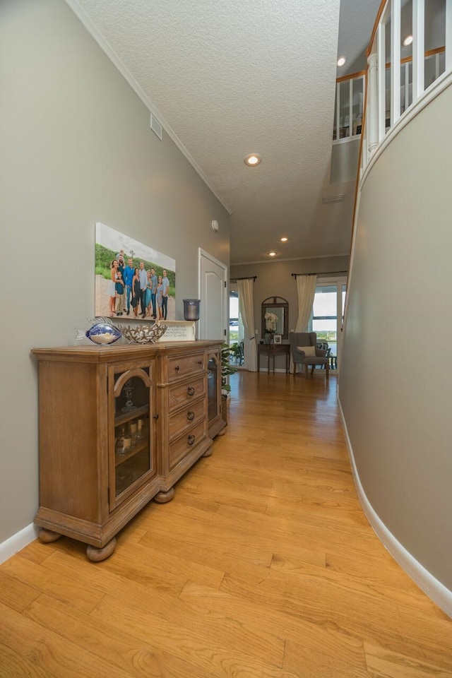 corridor featuring crown molding, light hardwood / wood-style floors, and a textured ceiling