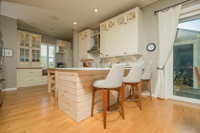 kitchen with a breakfast bar, white cabinets, wall chimney exhaust hood, decorative backsplash, and ornamental molding