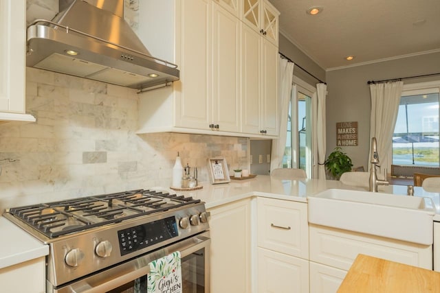 kitchen with wall chimney range hood, sink, decorative backsplash, ornamental molding, and stainless steel range