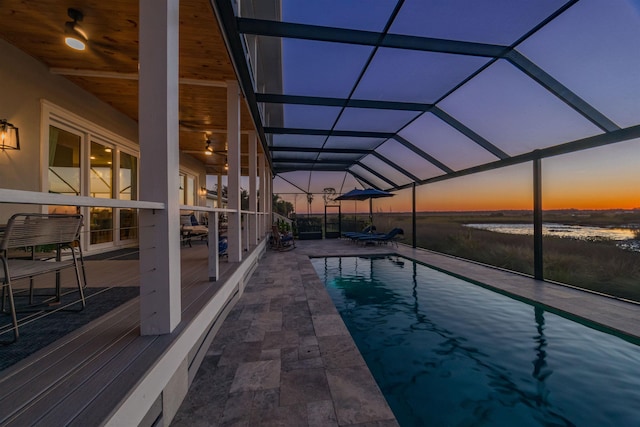 pool at dusk with glass enclosure and a patio area