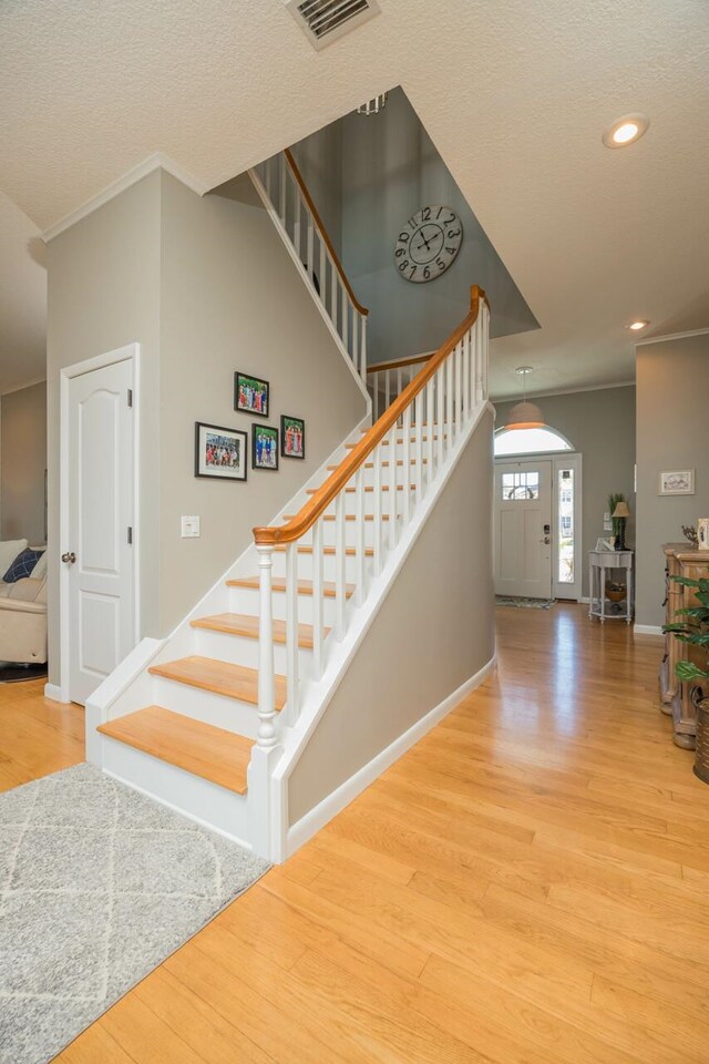 stairway featuring a textured ceiling, wood-type flooring, and ornamental molding