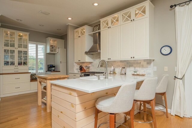 kitchen featuring white cabinetry, wall chimney exhaust hood, kitchen peninsula, a kitchen bar, and decorative backsplash