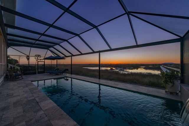 pool at dusk featuring a lanai, a water view, and a patio