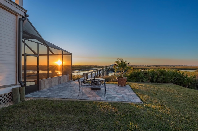 yard at dusk with a patio area, a water view, and glass enclosure