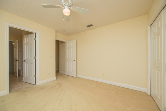 unfurnished bedroom featuring light carpet, a textured ceiling, a closet, and ceiling fan