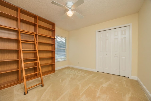 unfurnished bedroom featuring light carpet, a textured ceiling, a closet, and ceiling fan