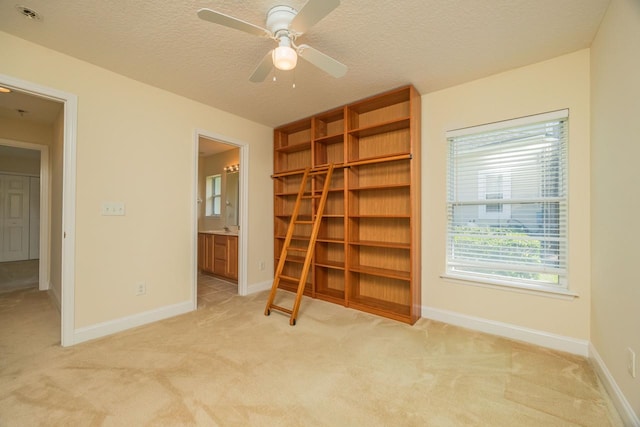 unfurnished bedroom with connected bathroom, light carpet, ceiling fan, and a textured ceiling