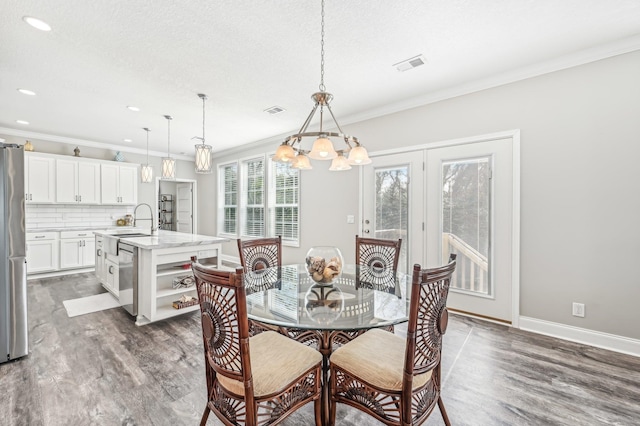 dining room with dark wood-type flooring, an inviting chandelier, sink, ornamental molding, and a textured ceiling