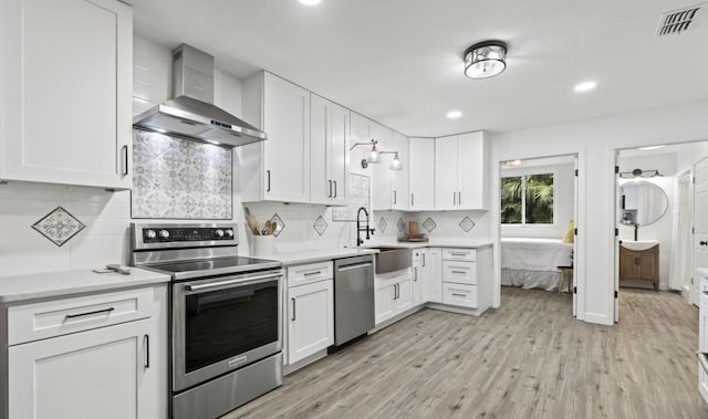 kitchen with appliances with stainless steel finishes, sink, white cabinets, wall chimney range hood, and decorative backsplash