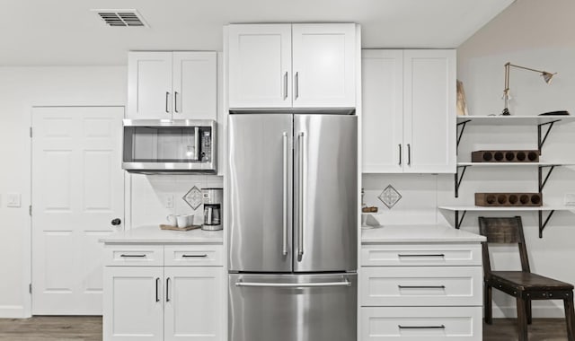 kitchen featuring wood-type flooring, backsplash, white cabinetry, and appliances with stainless steel finishes