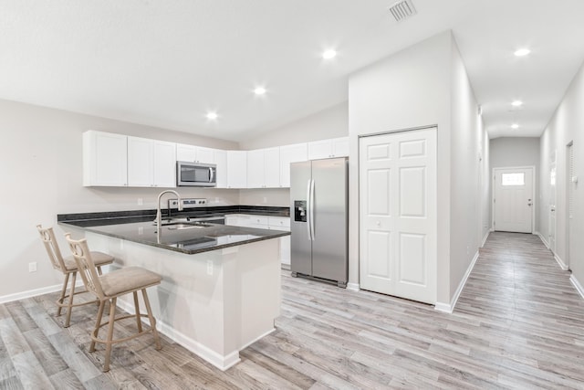 kitchen with white cabinetry, stainless steel appliances, a kitchen breakfast bar, kitchen peninsula, and light hardwood / wood-style floors