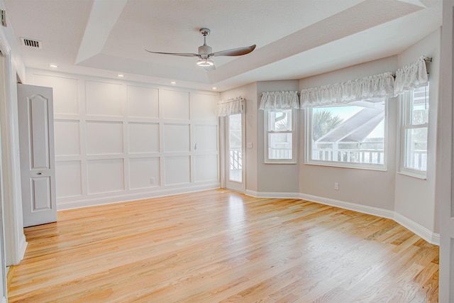 spare room with a raised ceiling, ceiling fan, and light wood-type flooring