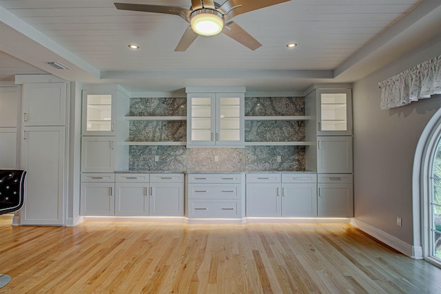 kitchen featuring white cabinetry, light stone countertops, light hardwood / wood-style floors, and a raised ceiling