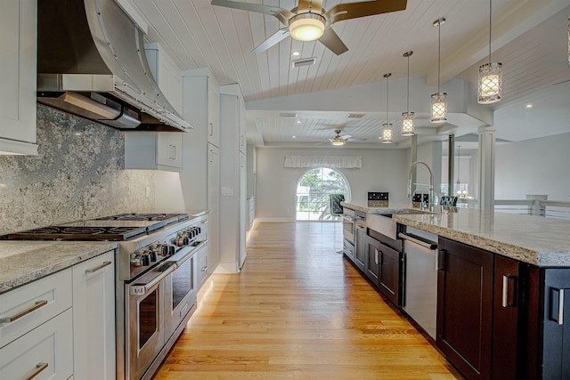 kitchen with ornate columns, sink, dark brown cabinetry, stainless steel appliances, and wall chimney exhaust hood