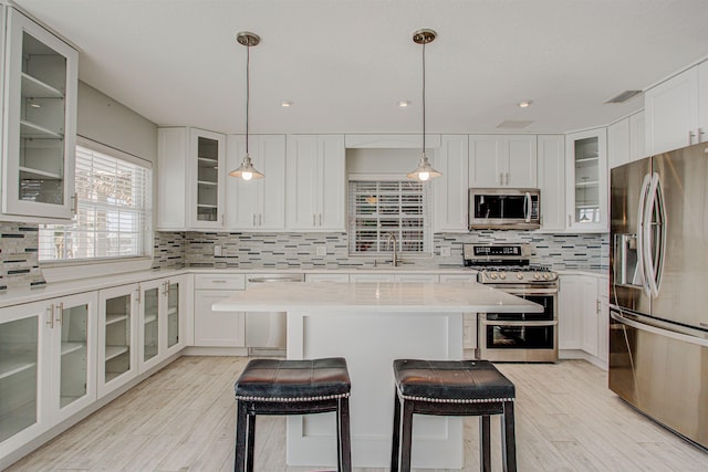 kitchen featuring appliances with stainless steel finishes, backsplash, white cabinets, a kitchen breakfast bar, and a center island