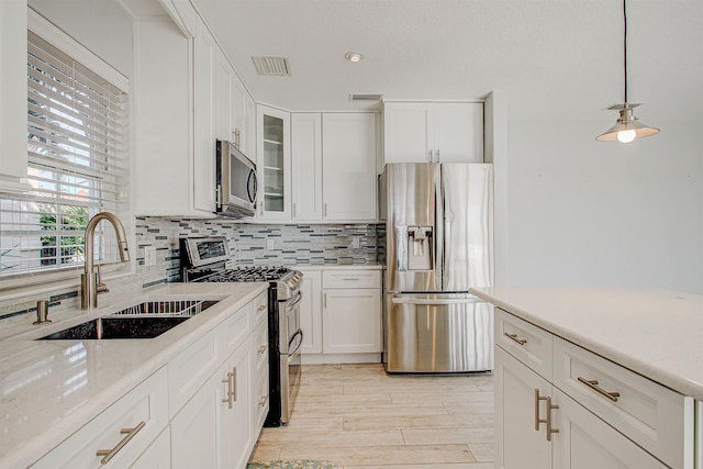 kitchen featuring tasteful backsplash, white cabinetry, sink, hanging light fixtures, and stainless steel appliances