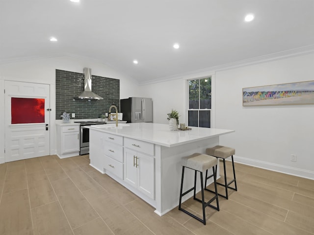 kitchen with stainless steel appliances, white cabinetry, light countertops, wall chimney exhaust hood, and a center island with sink