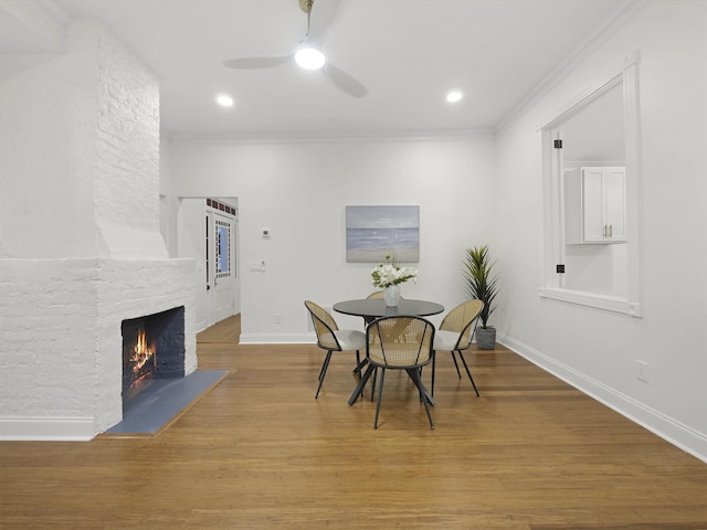 dining space with baseboards, ceiling fan, wood finished floors, crown molding, and a fireplace