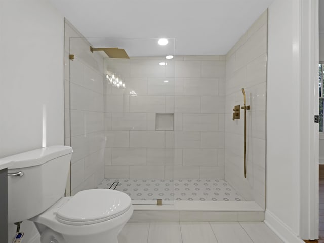 bathroom with baseboards, a tile shower, and toilet